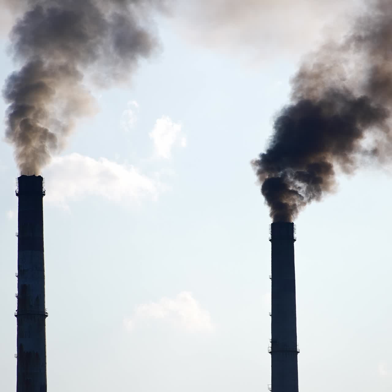 Dark silhouettes of factory pipes producing dark smoke into the sky. Air pollution from industry. Light blue sky backdrop