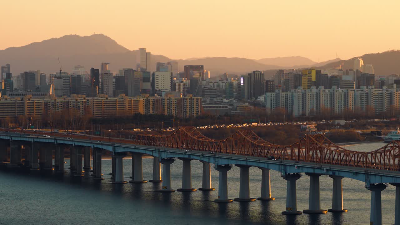 Ripresa aerea statica del traffico automobilistico intenso sul ponte Dongho con densi grattacieli di uffici e appartamenti residenziali nel distretto di Gangnam sotto un caldo cielo arancione al tramonto a Seoul, Corea del Sud