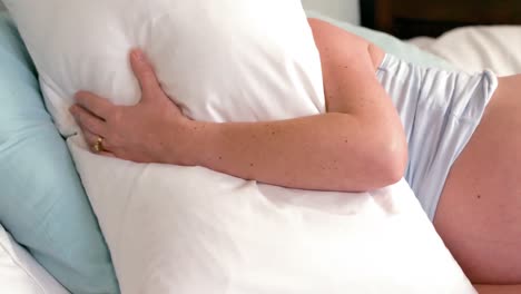 Pregnant-woman-laying-on-bed-covering-her-face-with-pillow