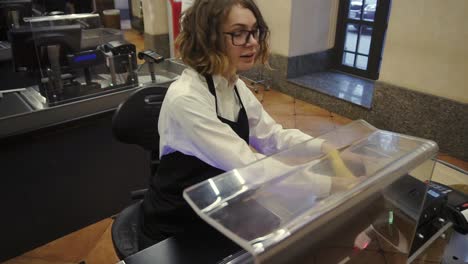 Cheerful-caucasian-saleswoman-in-white-shirt-and-black-apron-scanning-product,-fruits-at-checkout-counter-in-bright-supermarket