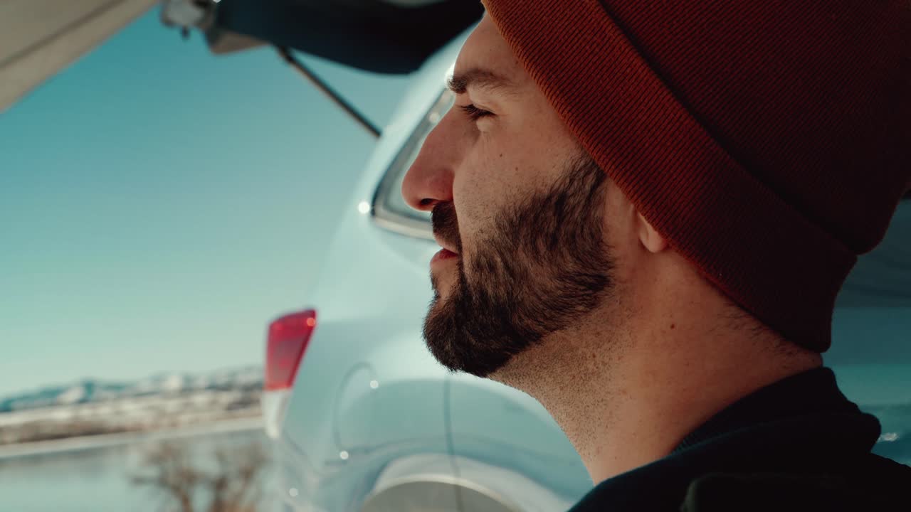 밀레니엄 세대 남성의 클로즈업은 캠핑 천막 아래에서 멋진 겨울 호수를 내려다보고 있습니다.