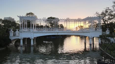 aerial dolly left of white bridge over pond at rosedal gardens in palermo neighborhood at golden hour, buenos aires