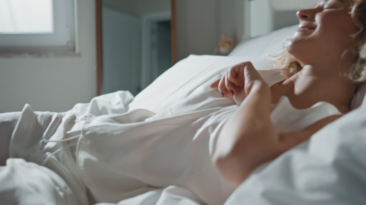 Woman legs jumping bed in sunlight closeup. Cheerful lady falling soft pillows