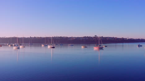 Yates-Y-Barcos-De-Lujo-Flotando-En-El-Lago-Sereno-Con-Reflejos-En-Un-Amanecer-En-Auckland,-Nueva-Zelanda