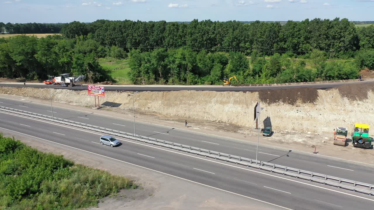 Cars and trucks on the highway. New road construction. Heavy machinery laying new asphalt road. Unfinished road near the highway in a sunny summer day. Top view.