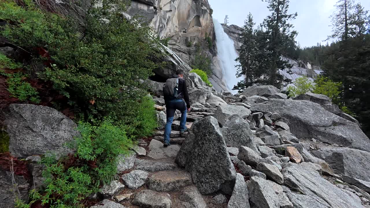 Uomo che fa escursioni in salita su un sentiero roccioso verso una cascata