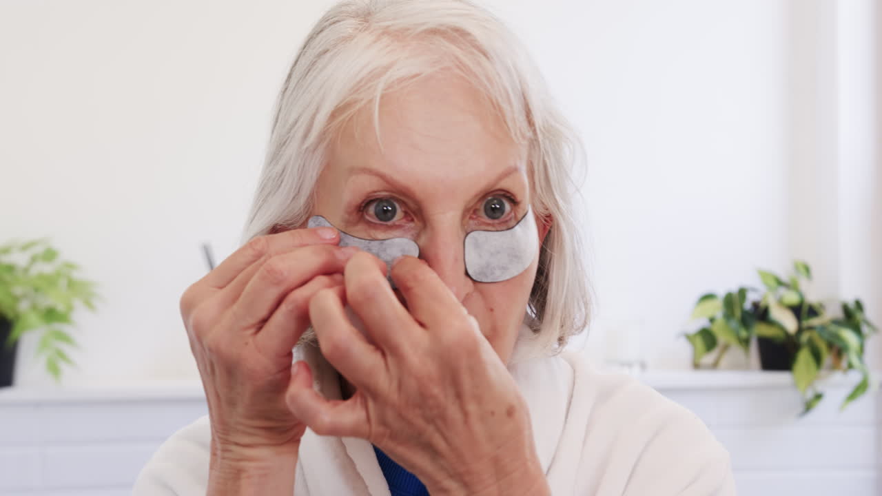 Senior woman applying under-eye patches at home for skincare routine