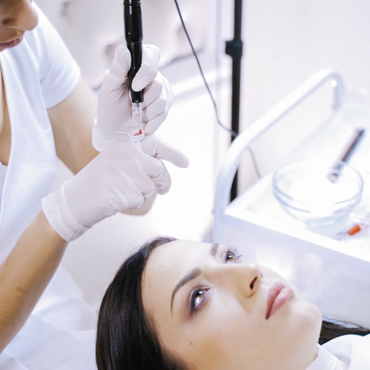 An experienced tattooist checks the work of the machine for permanent make-up in the presence of the client in the cosmetology before the procedure. Close-up.