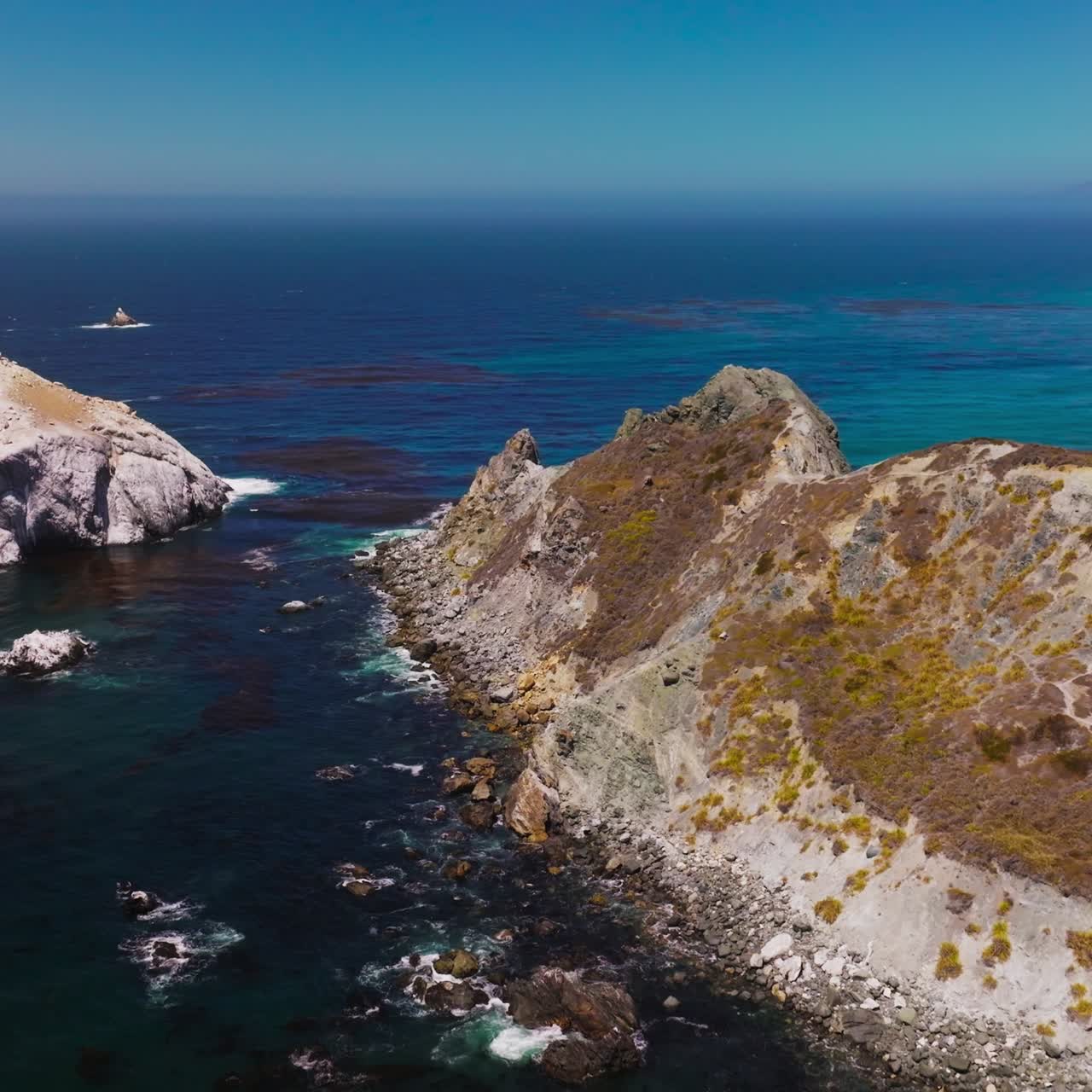 Rocks overgrown with moss surrounded by blue deep waters. Stunning seascape with hazy line of horizon on sunny day