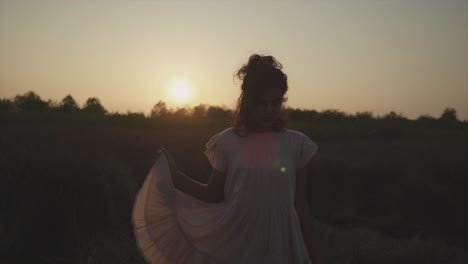 slow motion static shot of a young pretty indian woman standing on a field in nature during a beautiful sunset