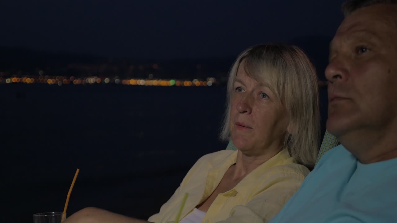 Casal de idosos relaxando com coquetéis na praia à noite