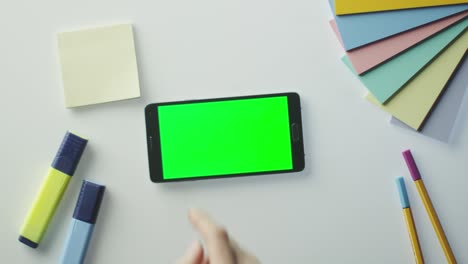 designer is using android phone with green screen in landscape mode. top view.