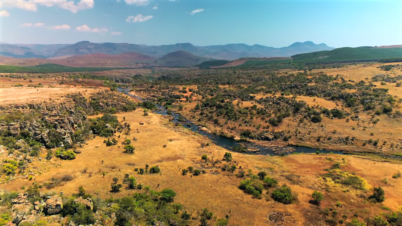 Scatto professionale dall'alto di un fiume che attraversa il vasto deserto roccioso della Namibia, mostrando il contrasto tra acqua e terreno arso dal sole.