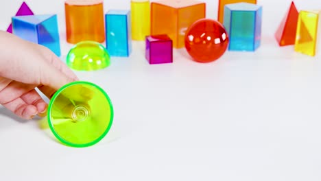 hands interact with colorful 3d geometric shapes on a white table, highlighting movement and structure under bright lighting