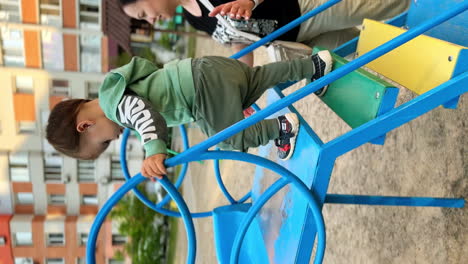cheerful caucasian toddler going down from a slide. mom secures her baby. time spent at playground. vertical screen.