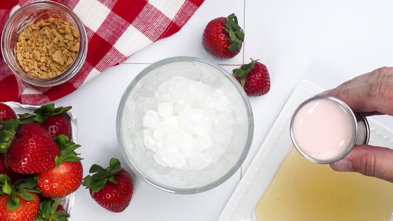 Making a Strawberry Shortcake Martini and adding in the strawberry liqueur with the other ingredients. Strawberries on a red and white gingham napkin. Close up of making a cocktail for happy hour.