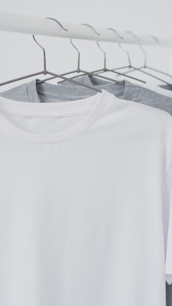 Vertical video of white and grey t shirts on hangers and copy space on white background