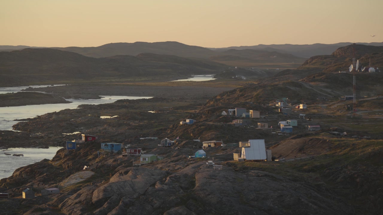 Wide landscape view capturing rustic hunting and fishing cabins clustered near the mouth of the Sylvia Grinnell River on the rocky outskirts of Iqaluit during late afternoon light.