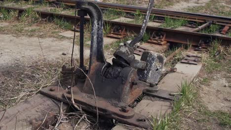 an old, rusty, oil-filled, manual railroad switch mechanism at an abandoned depot station. broken train cars. wooden sleepers