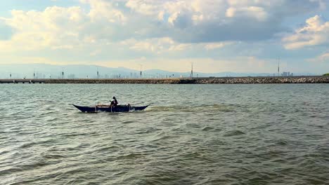 a lone fisherman rows across calm coastal waters with a city skyline backdrop and dramatic cloudscape, ideal for travel, solitude, or environmental themes