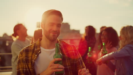 joyful guy having beer at sunset disco. multiethnic people having fun at party.