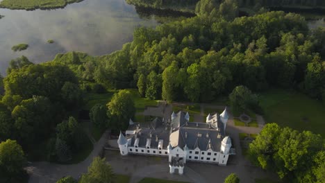 gorgeous aerial drone footage of a white majestic and large alatskivi castle in europe that sits by a large lake during a sunny day with treetops and green mowed lawn garden around. countryside castle