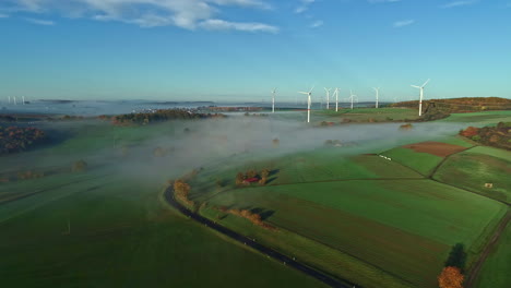 Luftdrohne-Vorwärts-Bewegte-Aufnahme-Von-Grünen-Ackerflächen-Und-Windmühlen-In-Gabsheim,-Rheinland-Pfalz,-Deutschland-An-Einem-Nebligen-Morgen