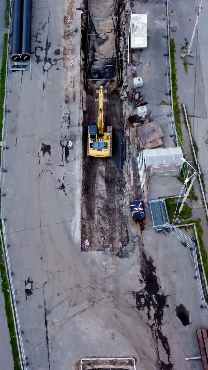 Yellow excavator digging on a construction site in Riga, aerial top-down view during daytime, vertical