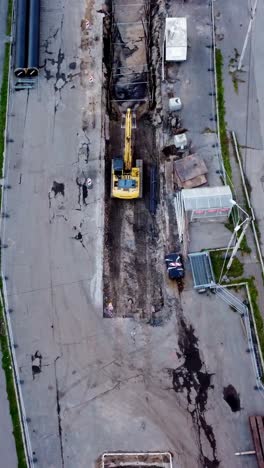 yellow excavator digging on a construction site in riga, aerial top-down view during daytime, vertical