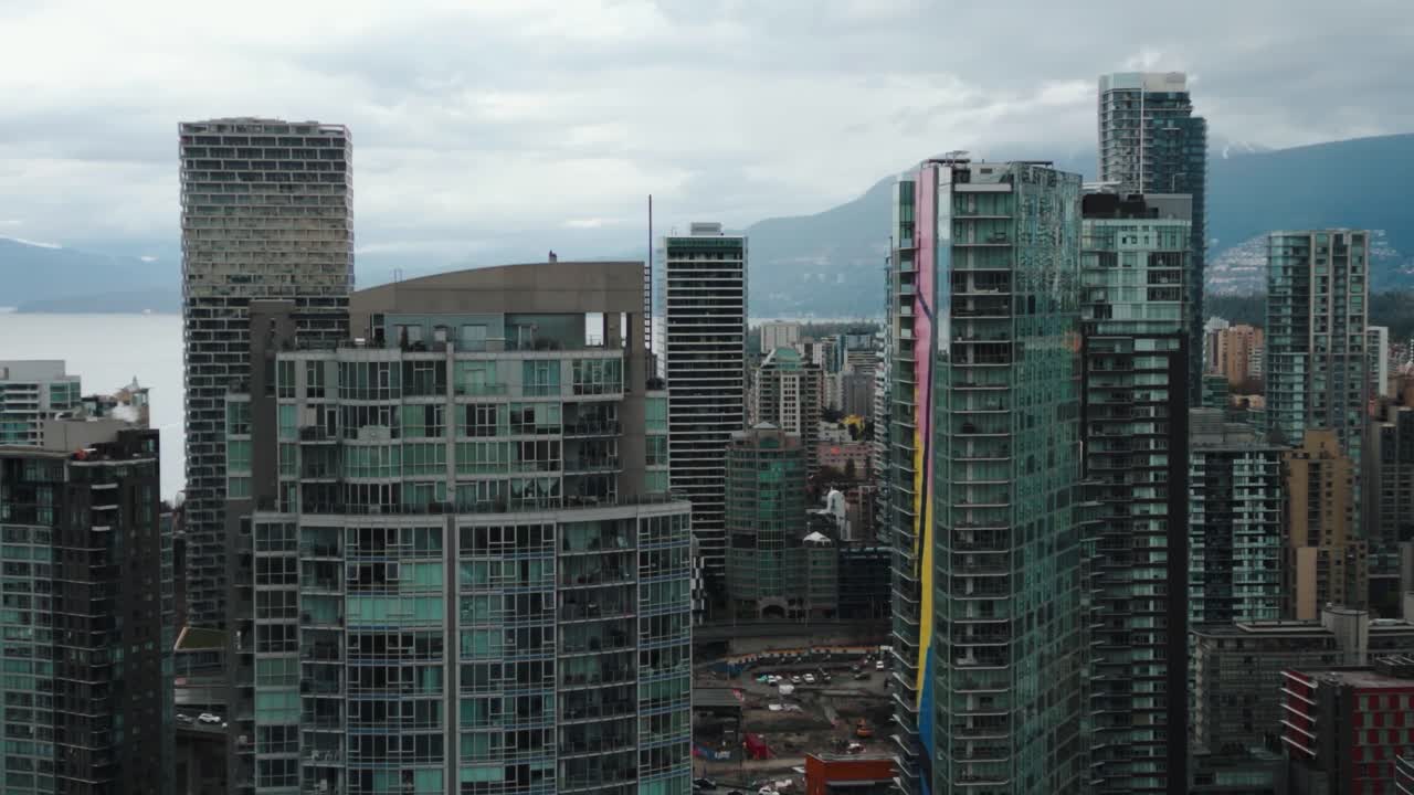 fotografía aérea de cerca yendo hacia atrás entre edificios en la ciudad de vancouver, yaletown, con montañas y océano en el fondo en un día nublado