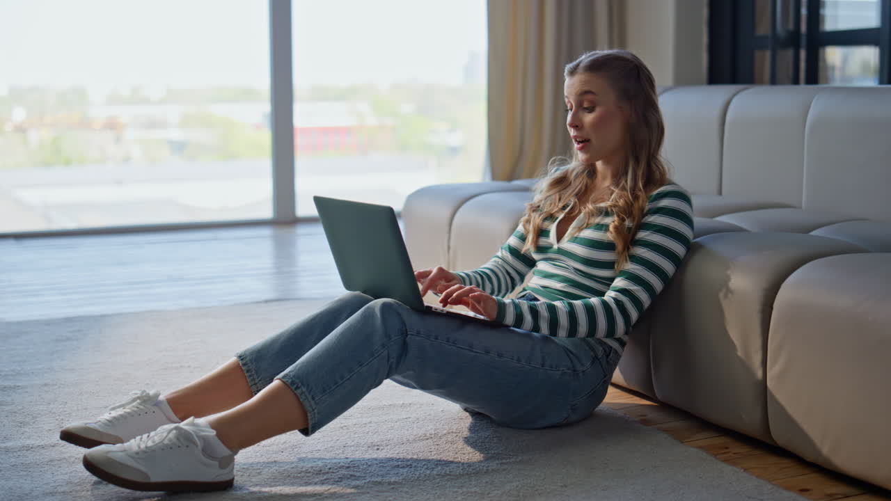 Thoughtful girl texting laptop in modern apartment. Pensive woman working online