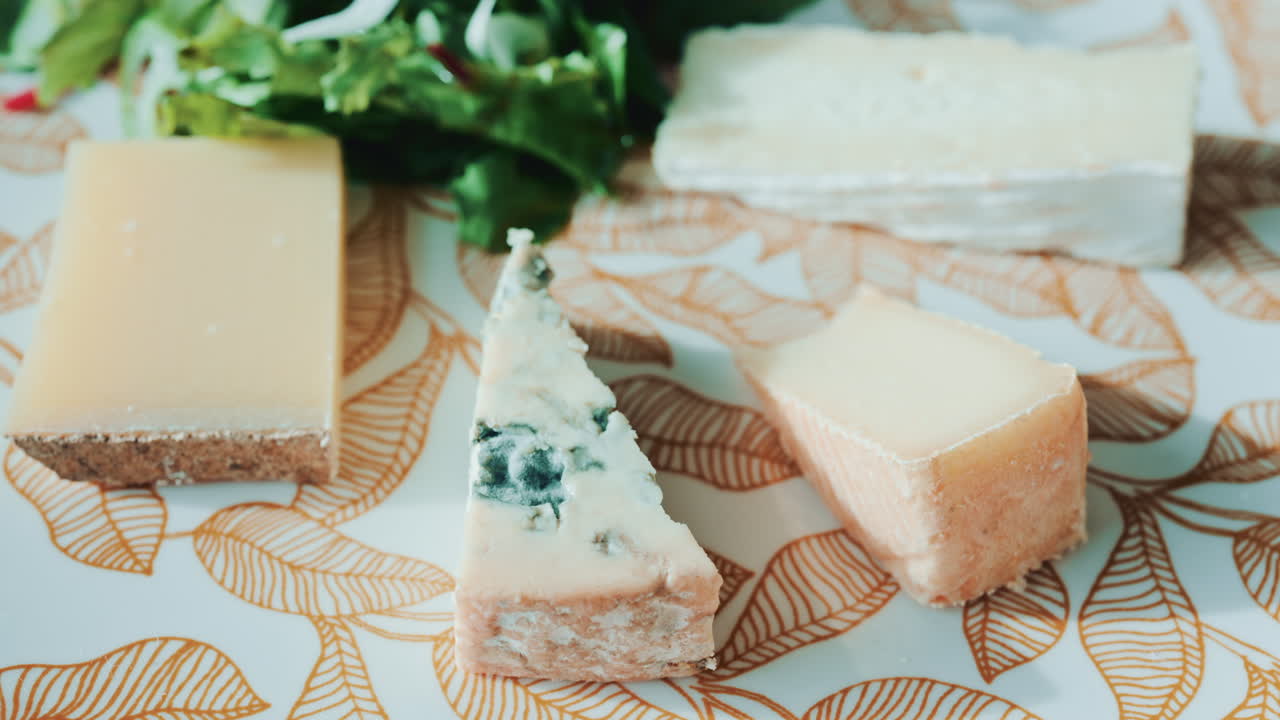 Close up of a cheese plate with assorted cheeses and salad on an elegant patterned plate