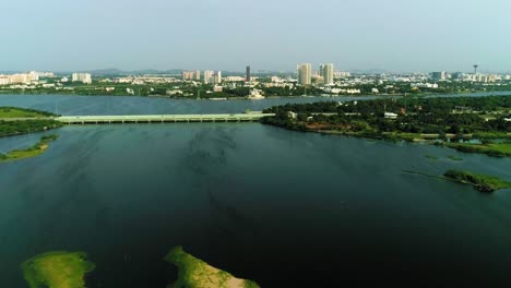 Drohnenaufnahmen-Eines-Strandes-Mit-Einem-Sich-öffnenden-Stauwasser-Und-Einer-Skyline-Der-Stadt-Mit-Hochhäusern-Im-Hintergrund