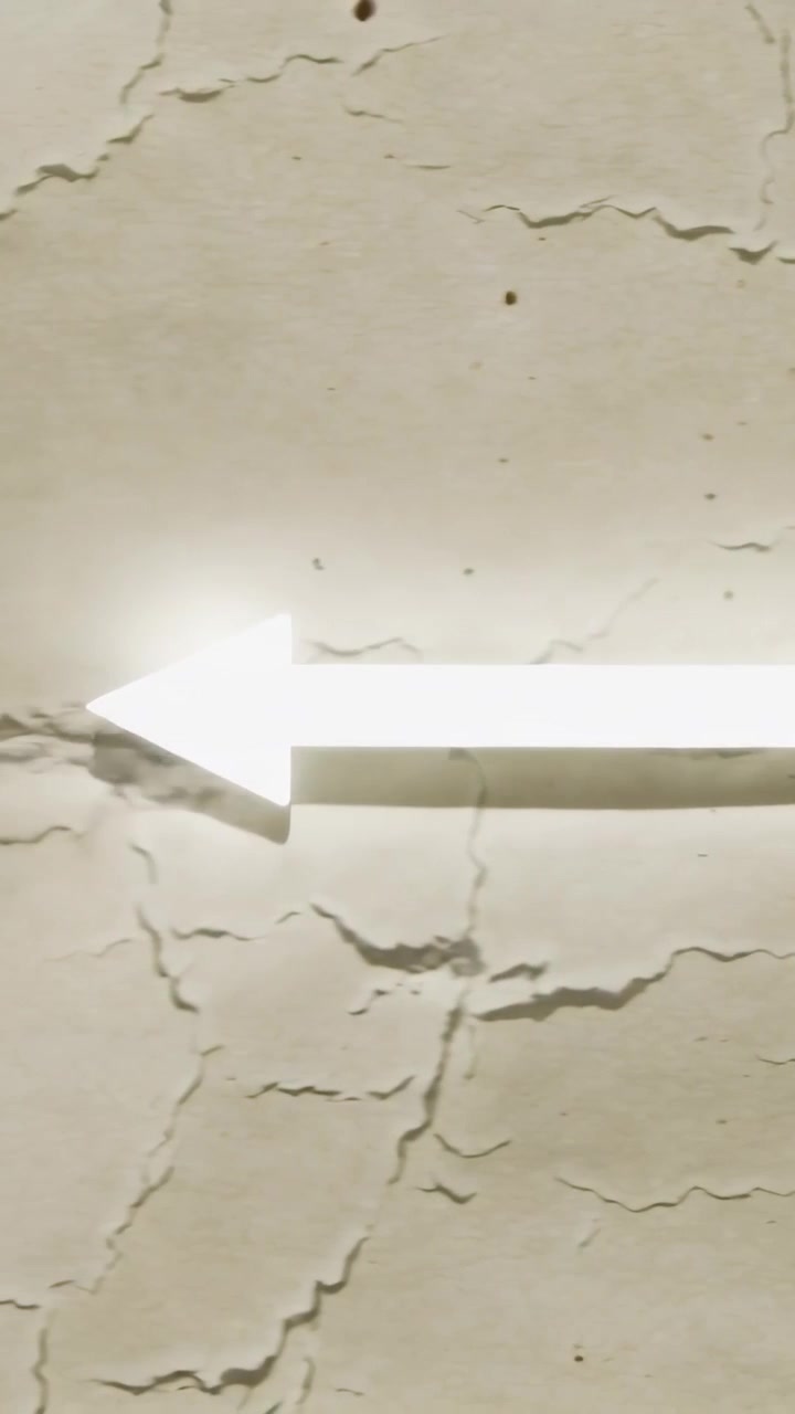 Video verticale: Segnale luminoso con freccia a sinistra che appare su una parete intonacata beige, dirigendo il traffico nel corridoio.