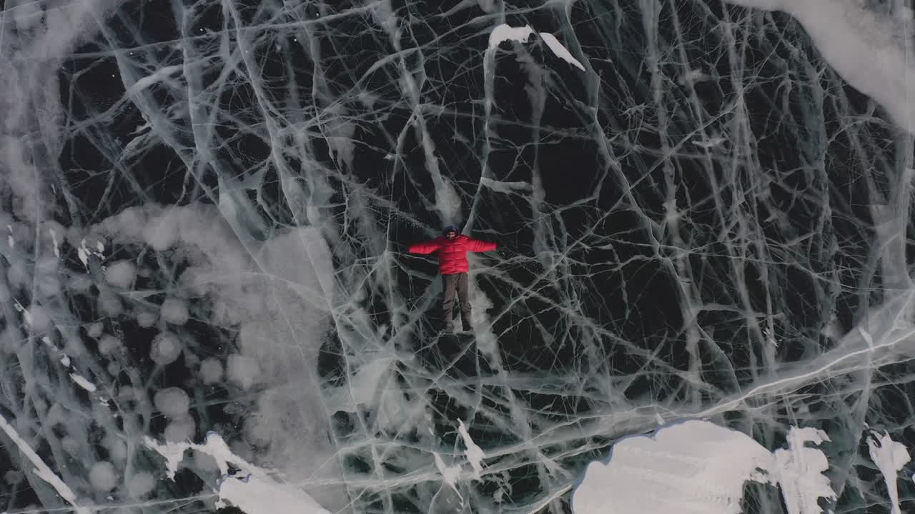 한 남자가 겨울에 얼음 위에 누워서 팔과 다리를 으로 펼쳐서 물에 떠 있는 척하고 천사를 묘사합니다.