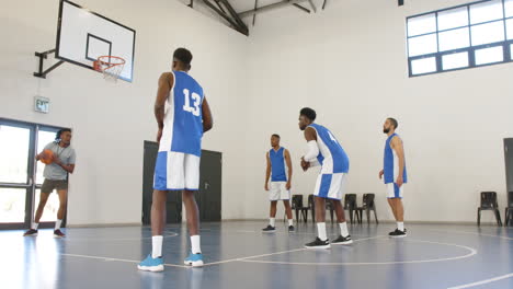 multiracial male basketball players with coach giving instructions in gym