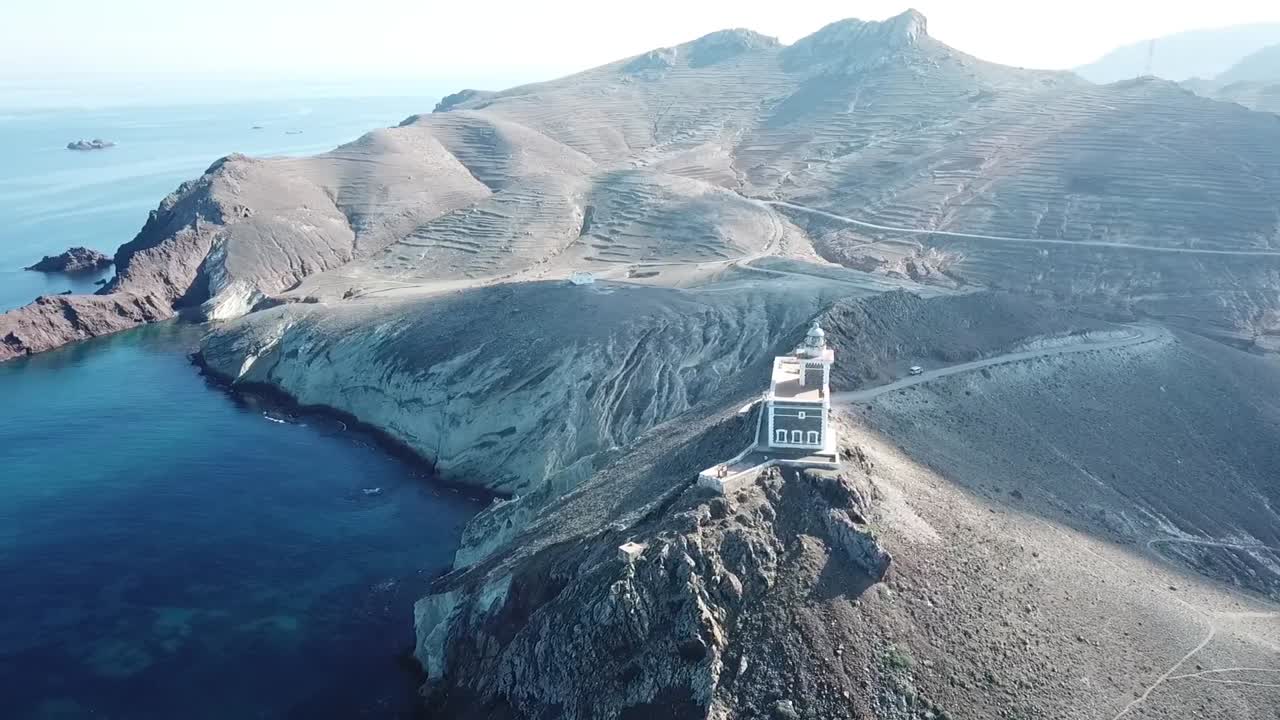 Cinematic drone shot orbiting a white lighthouse located on a steep rocky cliff edge overlooking the deep blue Mediterranean Sea
