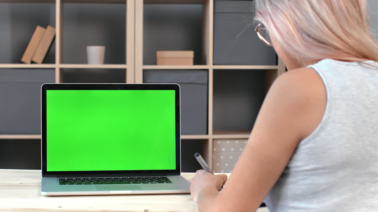vista posterior estudiante femenina haciendo notas en papel durante el aprendizaje electrónico educación en línea portátil pantalla verde