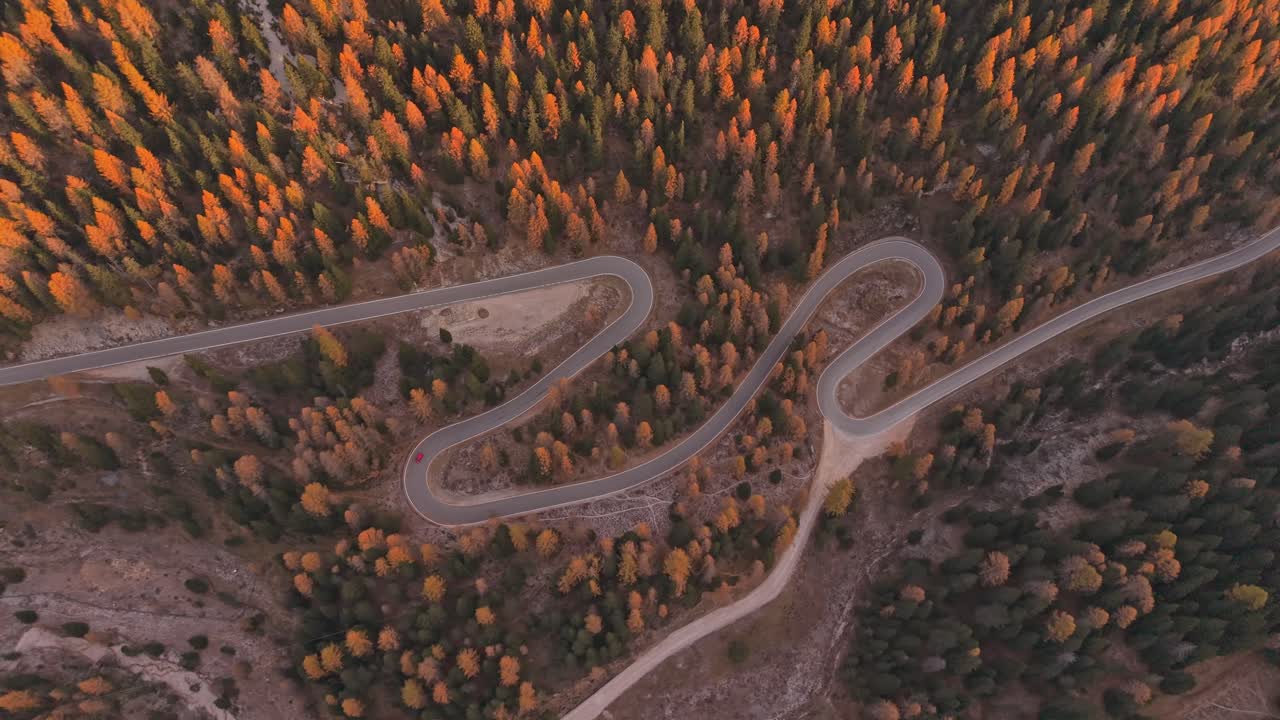 Sunrise aerial over curvy Dolomites road with fall trees and traffic