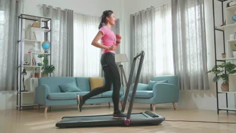 vista lateral de una mujer asiática corriendo en una cinta de correr en casa