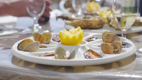 white seafood platter with half a lemon in the middle, on a light table with glasses of white wine