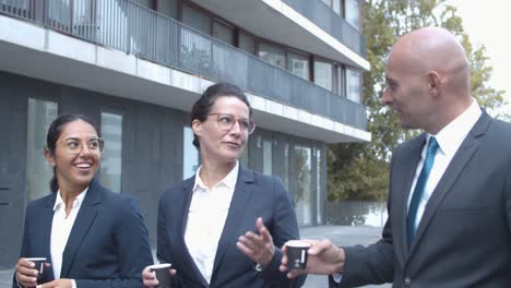 smiling confident business colleagues walking at office building, drinking coffee and talking together