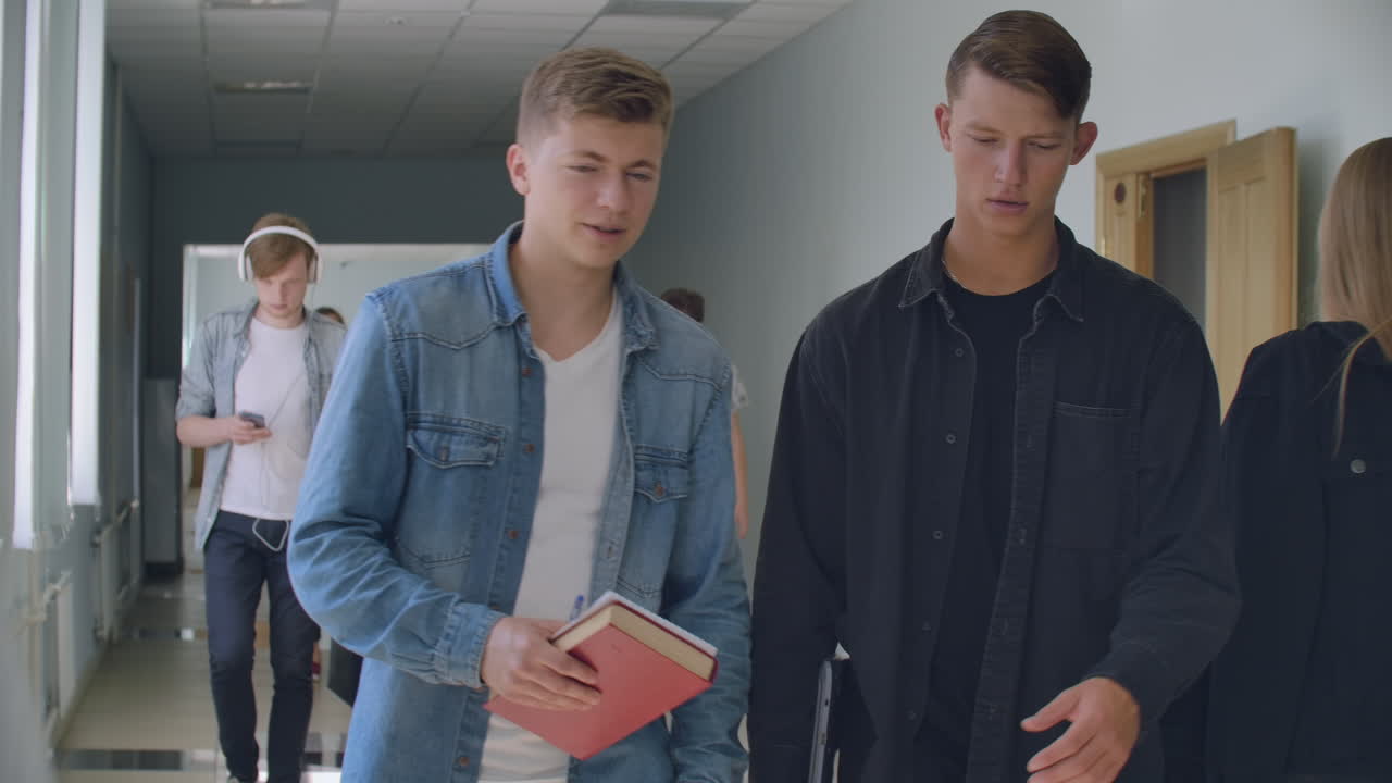estudiantes universitarios en el vestíbulo. mucha gente camina por el pasillo de la universidad hablando discutiendo y escuchando música. la cámara se mueve entre diferentes grupos