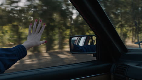 Frau-Hält-Die-Hand-Aus-Dem-Autofenster-Und-Spürt,-Wie-Der-Wind-Durch-Die-Finger-Weht,-Während-Sie-Auf-Dem-Land-Fährt-Und-Im-Sommerurlaub-Unterwegs-Ist-Und-Die-Freiheit-Auf-Der-Straße-Genießt