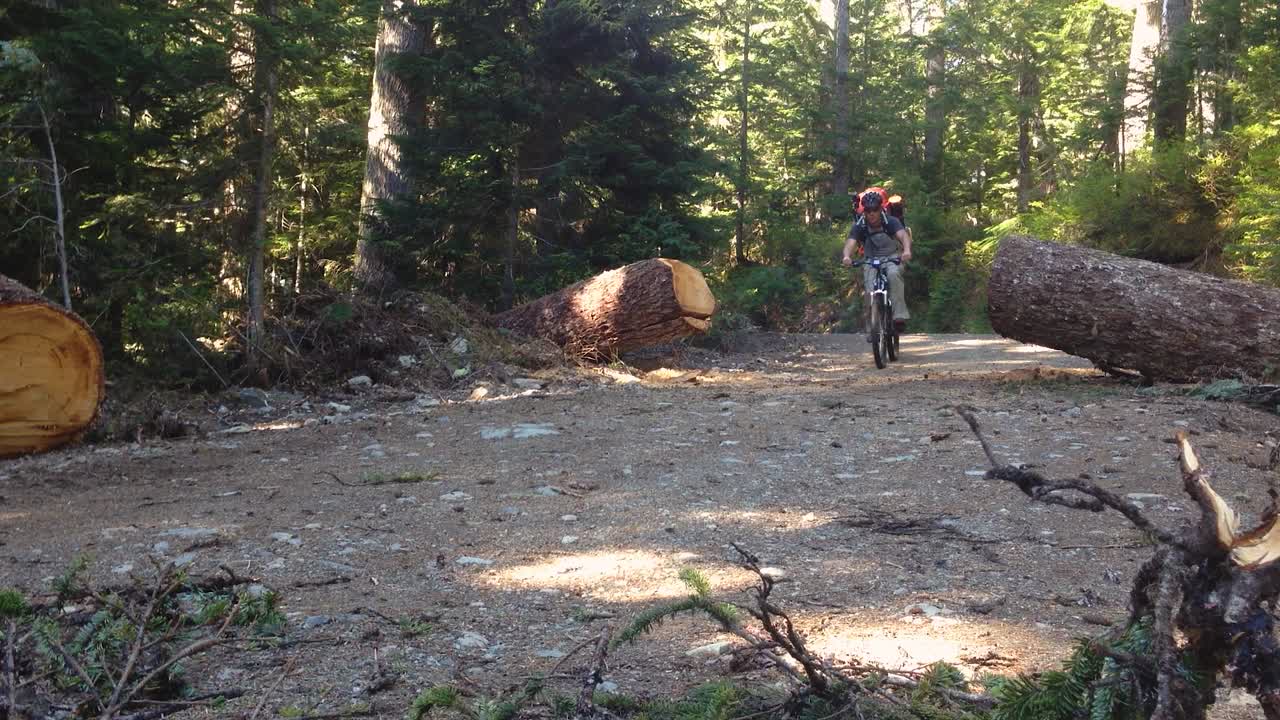 hombre montando su bicicleta de montaña por un sendero de grava de tierra en un parque arbolado usando un casco mochila de senderismo equipo de camping aventura