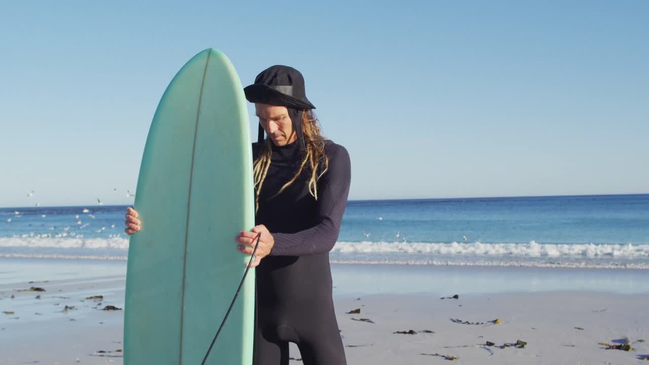 ⁇ 은 해변 에서 서핑 보드 를 들고 있는 웨이트 슈트 를 입은 드레드 로크 를 입은 웃는 백인 남성 의 비디오