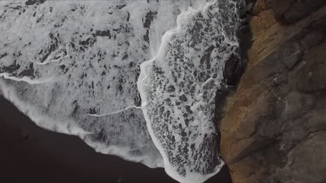 Vista-Aérea-De-Salpicaduras-Y-Swashes-De-Olas-En-Las-Rocas-De-Los-Acantilados-En-La-Playa-Volcánica-A-Orillas-Del-Mar