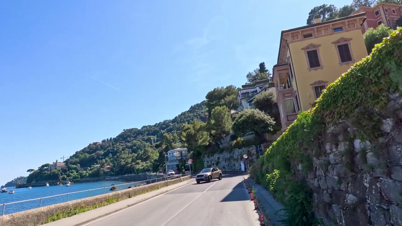 Una carrellata dal basso segue un veicolo che percorre una tortuosa strada costiera mediterranea.