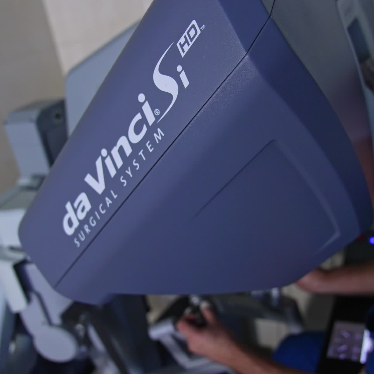 Surgical system Da Vinci is operated by the experienced medic in blue uniform. Male surgeon sits at the desk control of the equipment moving the levers