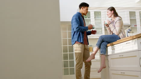 happy diverse couple talking and drinking coffee in kitchen at home, copy space, in slow motion